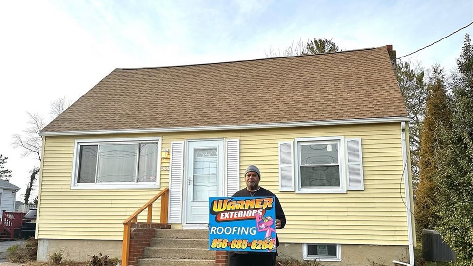 Homeowner holding Warner Exteriors roofing sign after roof replacement project.