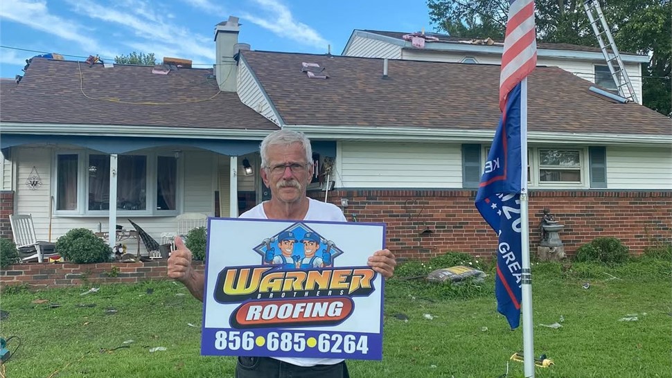 Homeowner holding Warner Exteriors roofing sign in front of house