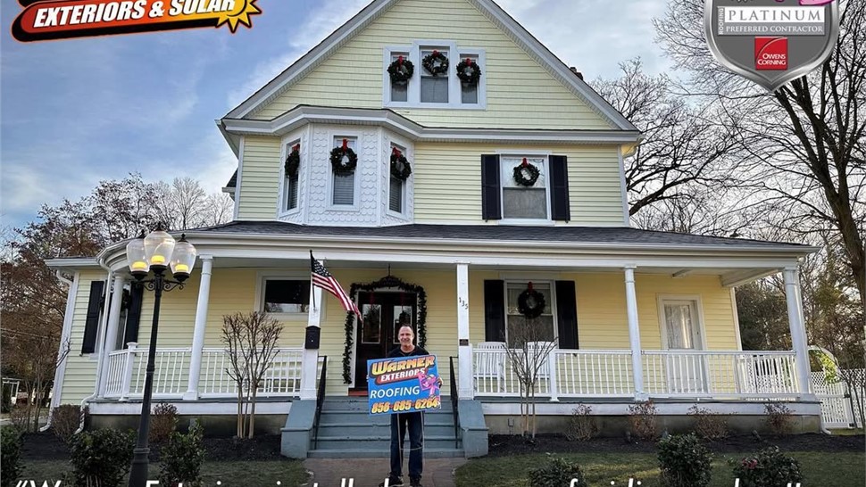 Customer standing in front of a yellow home after roof and siding installation by Warner Exteriors.