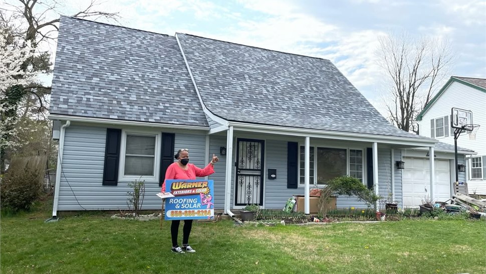 Customer holding Warner Exteriors roofing sign beside home