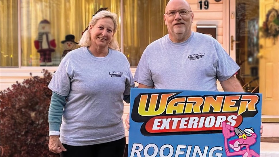 Smiling homeowners holding Warner Exteriors roofing sign after project completion
