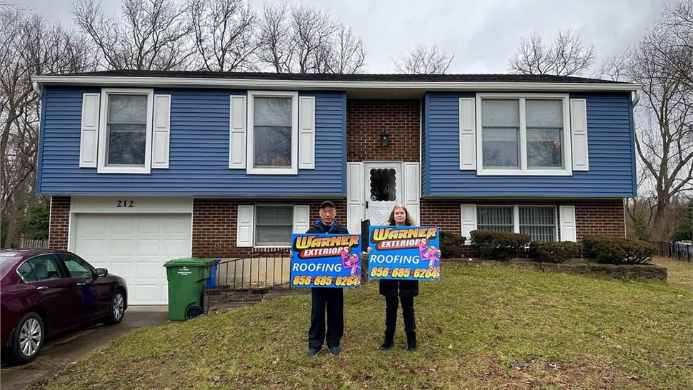 Two homeowners holding Warner Exteriors roofing sign after roof replacement