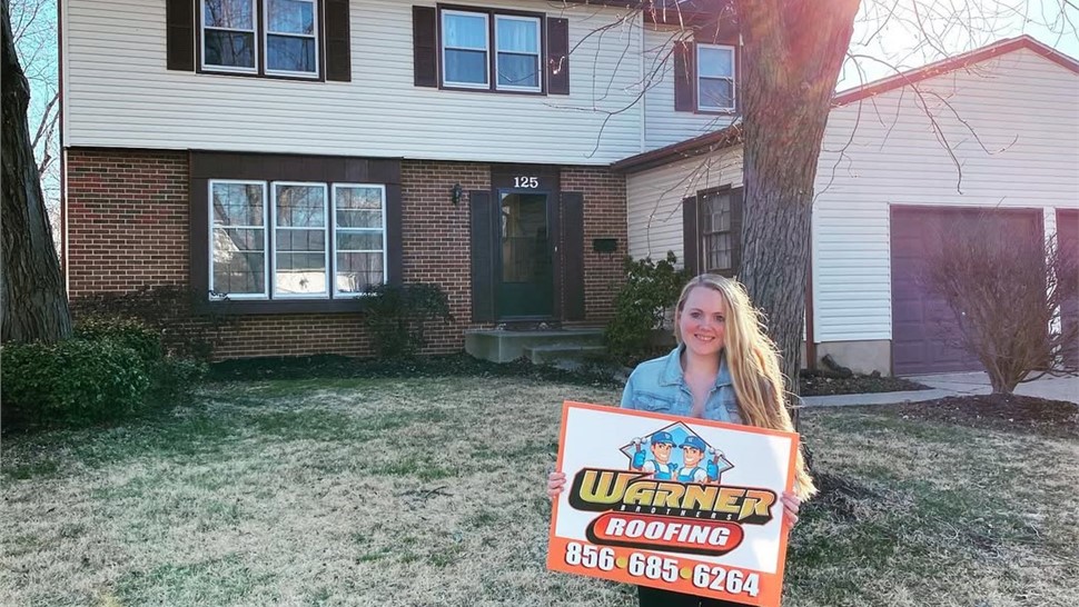 Customer holding Warner Exteriors roofing sign in front of home