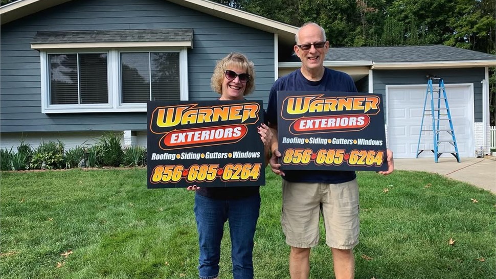 Homeowners standing in yard with Warner Exteriors roofing sign