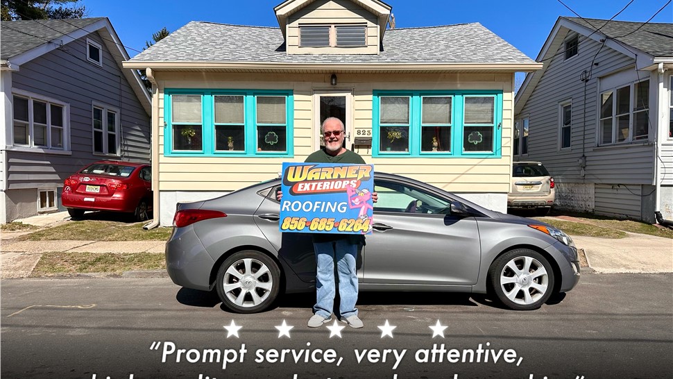 Customer holding Warner Exteriors sign in front of newly roofed home
