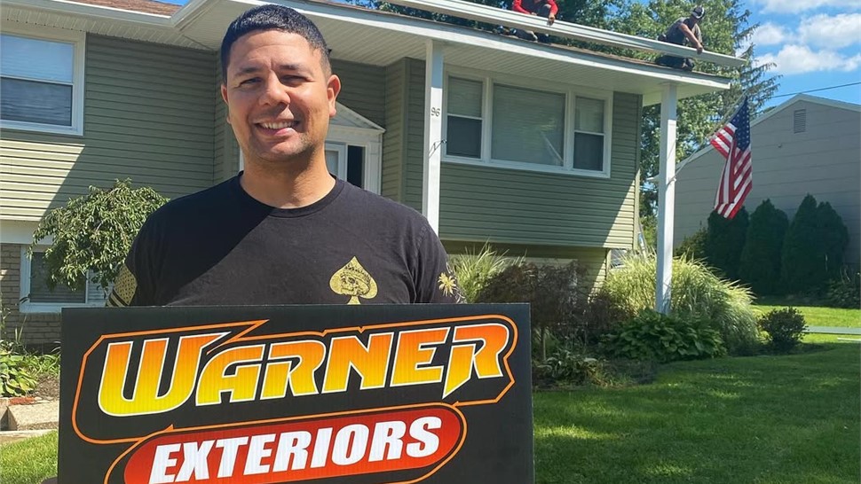 Happy customer holding Warner Exteriors sign after home exterior project