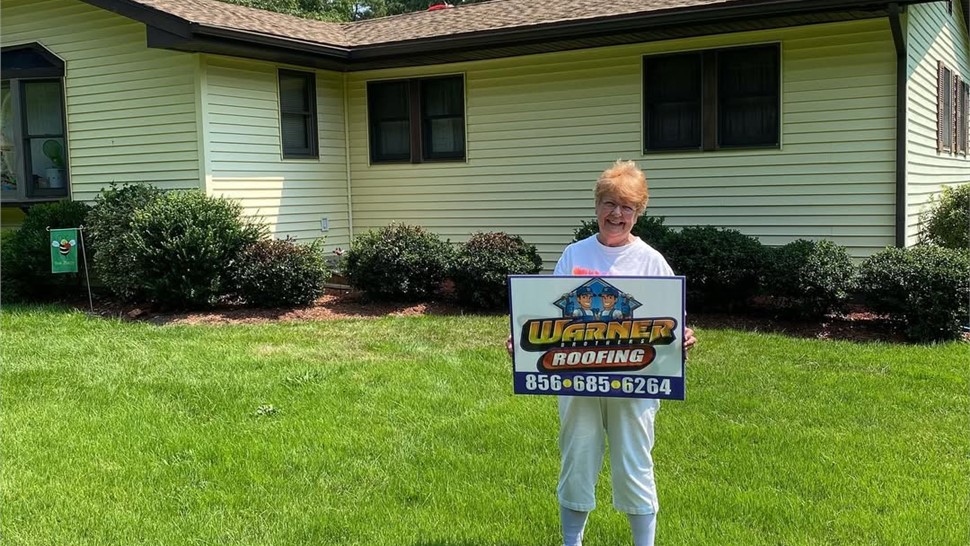 Senior homeowner holding Warner Exteriors roofing sign after installation
