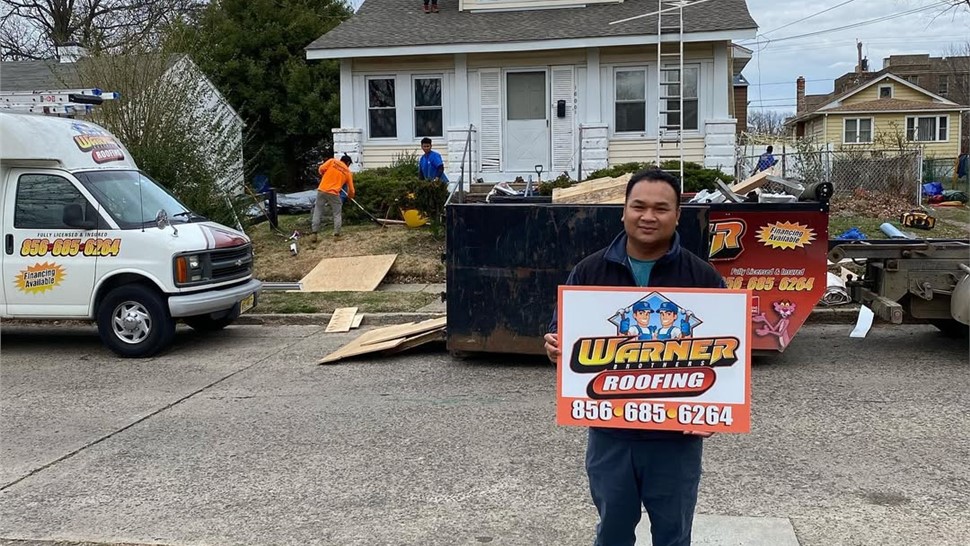 Customer holding Warner Exteriors roofing sign near home exterior