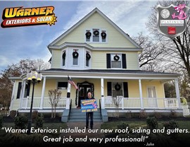 Customer standing in front of a yellow home after roof and siding installation by Warner Exteriors.