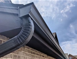 Black seamless gutter system with matching downspout installed on brick and siding home in New Jersey