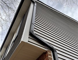 Black seamless gutters and downspouts installed on gray vinyl siding home in New Jersey