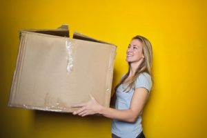 Blonde woman holding moving box against yellow background