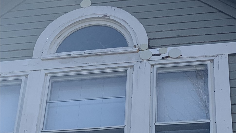 Cracked and peeling trim around an arched gable window in Fort Collins