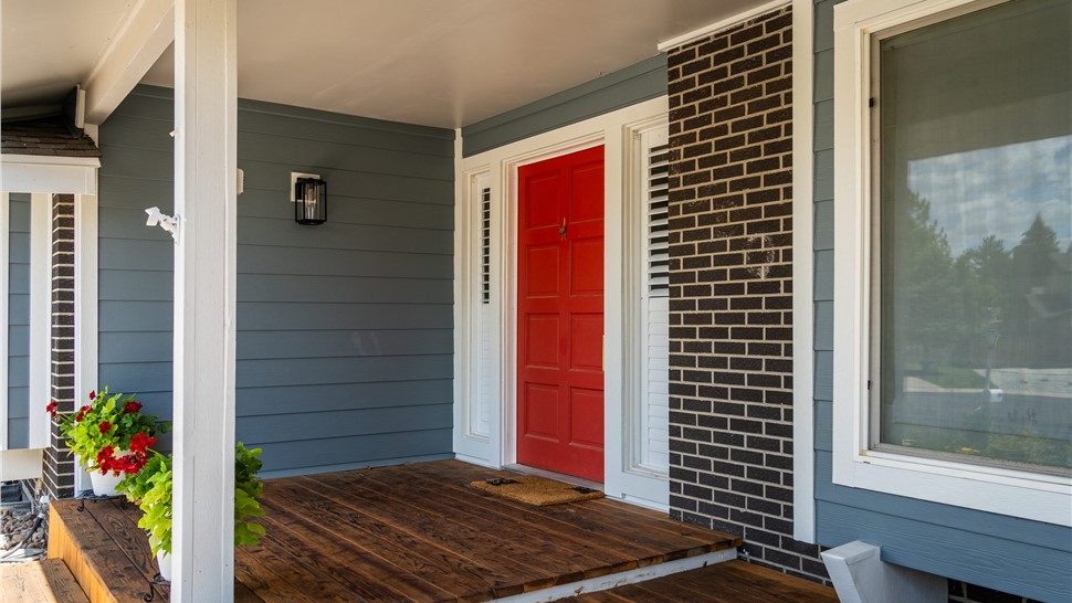Covered front porch with red door, Boothbay Blue lap siding, and white trim beside a dark brick column in Longmont
