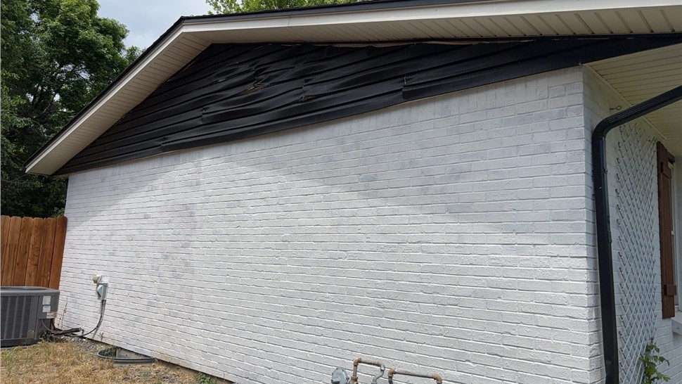 Peeling, sagging painted vinyl siding on a Longmont home's gable before replacement