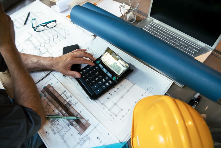 person at a desk with blueprints and a calculator